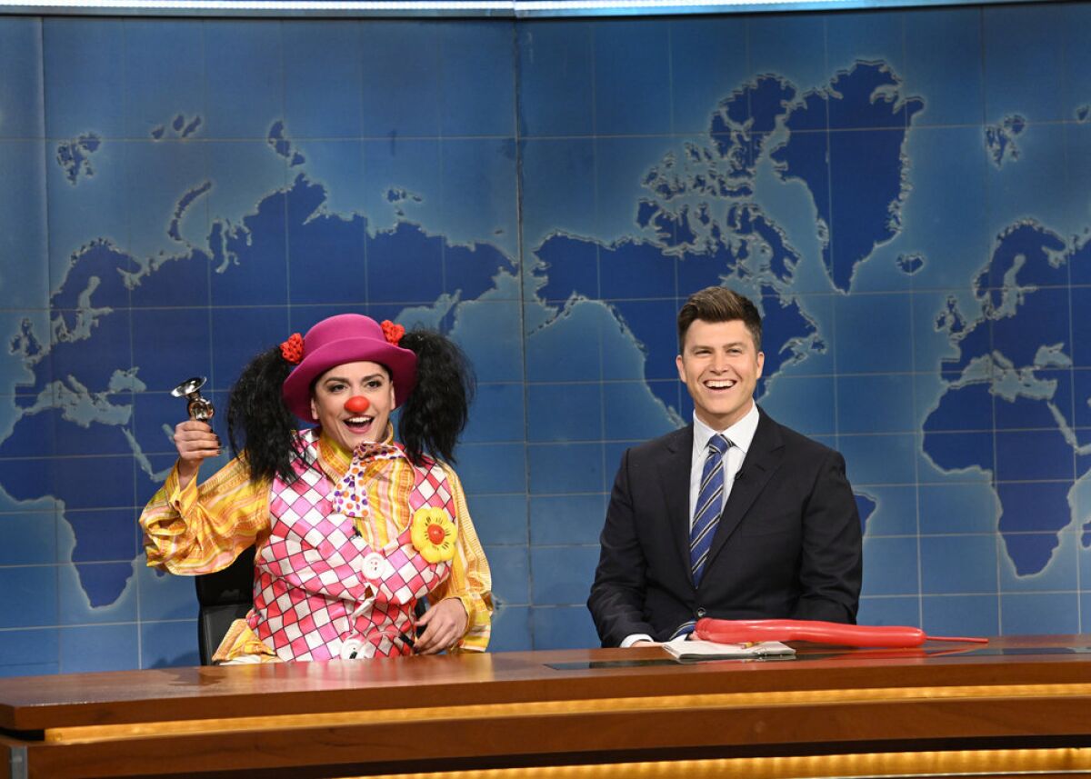 A woman in a clown costume and a man in a suit sitting behind a news desk