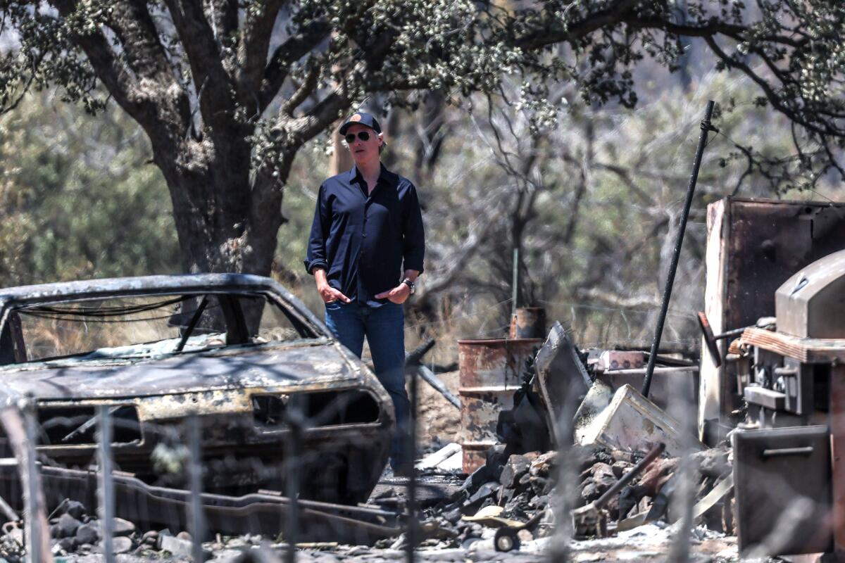 A man stands near a burned car among fire debris.