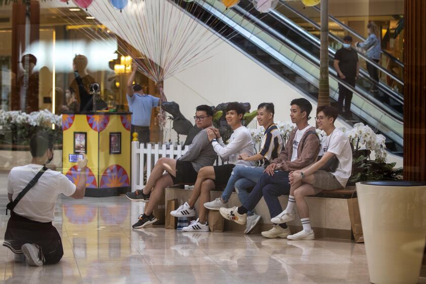 COSTA MESA, CA - MAY 13, 2021: A group of shoppers take off their masks to pose for a photo across from the carousel inside South Coast Plaza on May 13, 2021 in Costa Mesa, California. Even though, the CDC announced Thursday that masked are no longer required for fully vaccinated people, the mall is still requiring masks indoors.(Gina Ferazzi / Los Angeles Times)