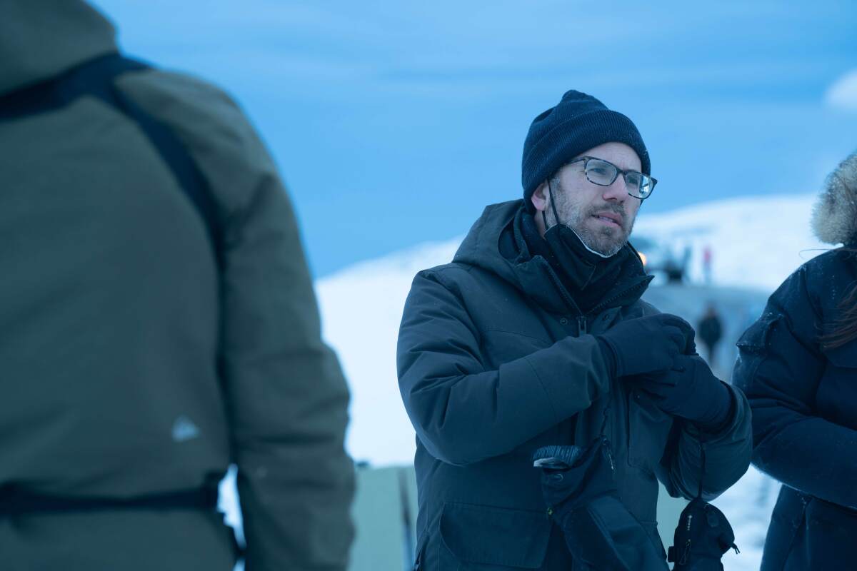 Alex DiGerlando in a coat and beanie with a mask around his chin on a set in Iceland.