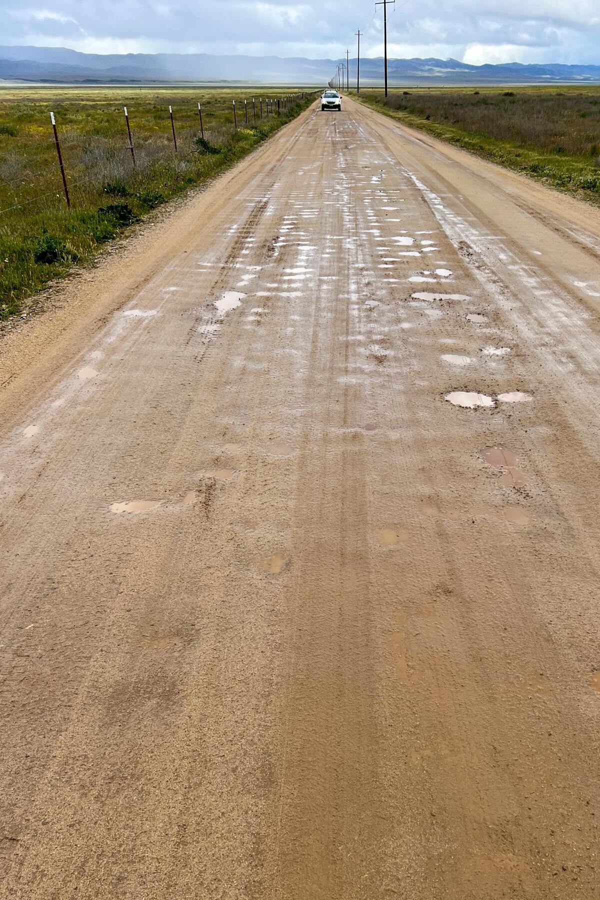 A vertical photograph of a long, straight, muddy dirt road.