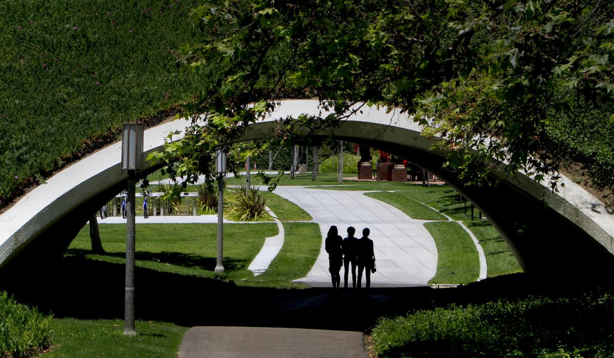 Three people, in silhouette, walk under an arch in an area with lawns and paths 