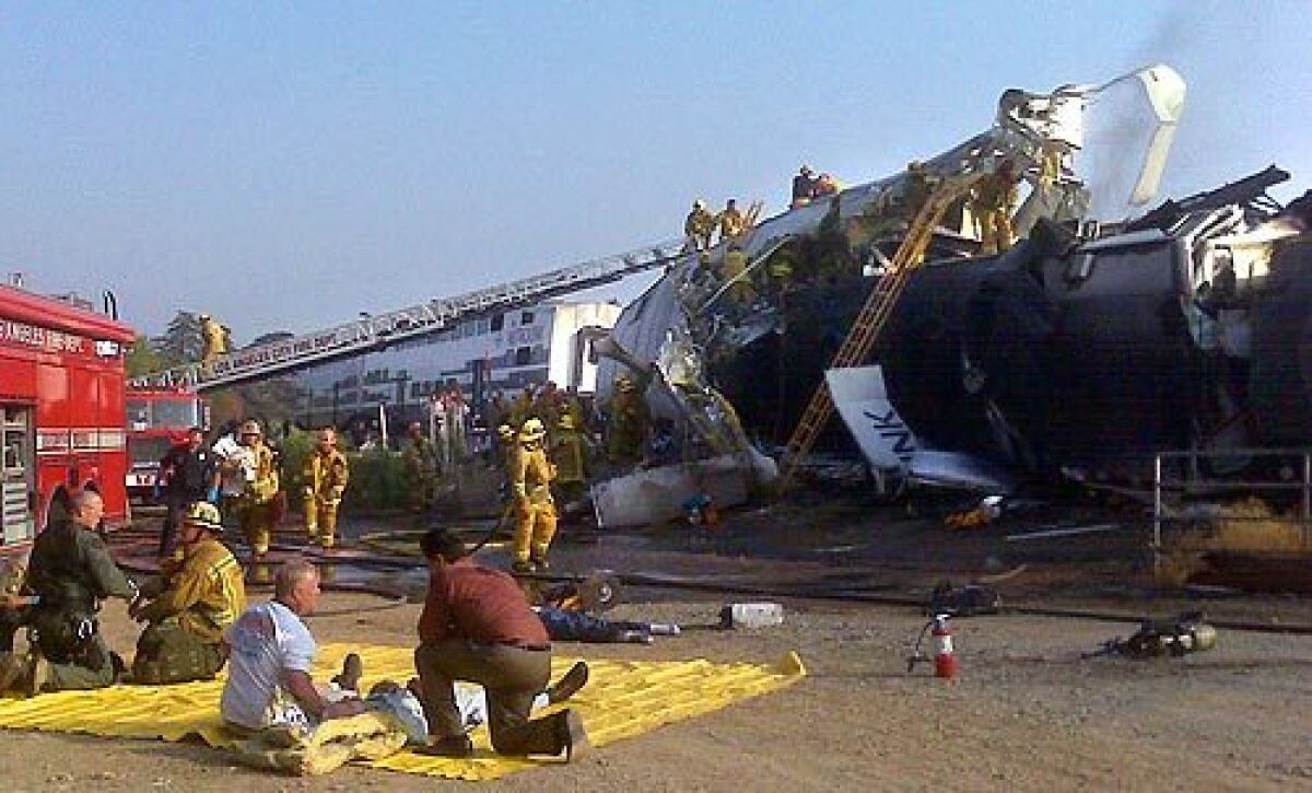 Firefighters treat people on yellow tarps next to the wreckage of a crashed train