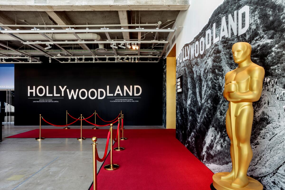  Entrance of an exhibition at the Academy Museum with a sign that says "Hollywoodland" and a large Oscars statue. 