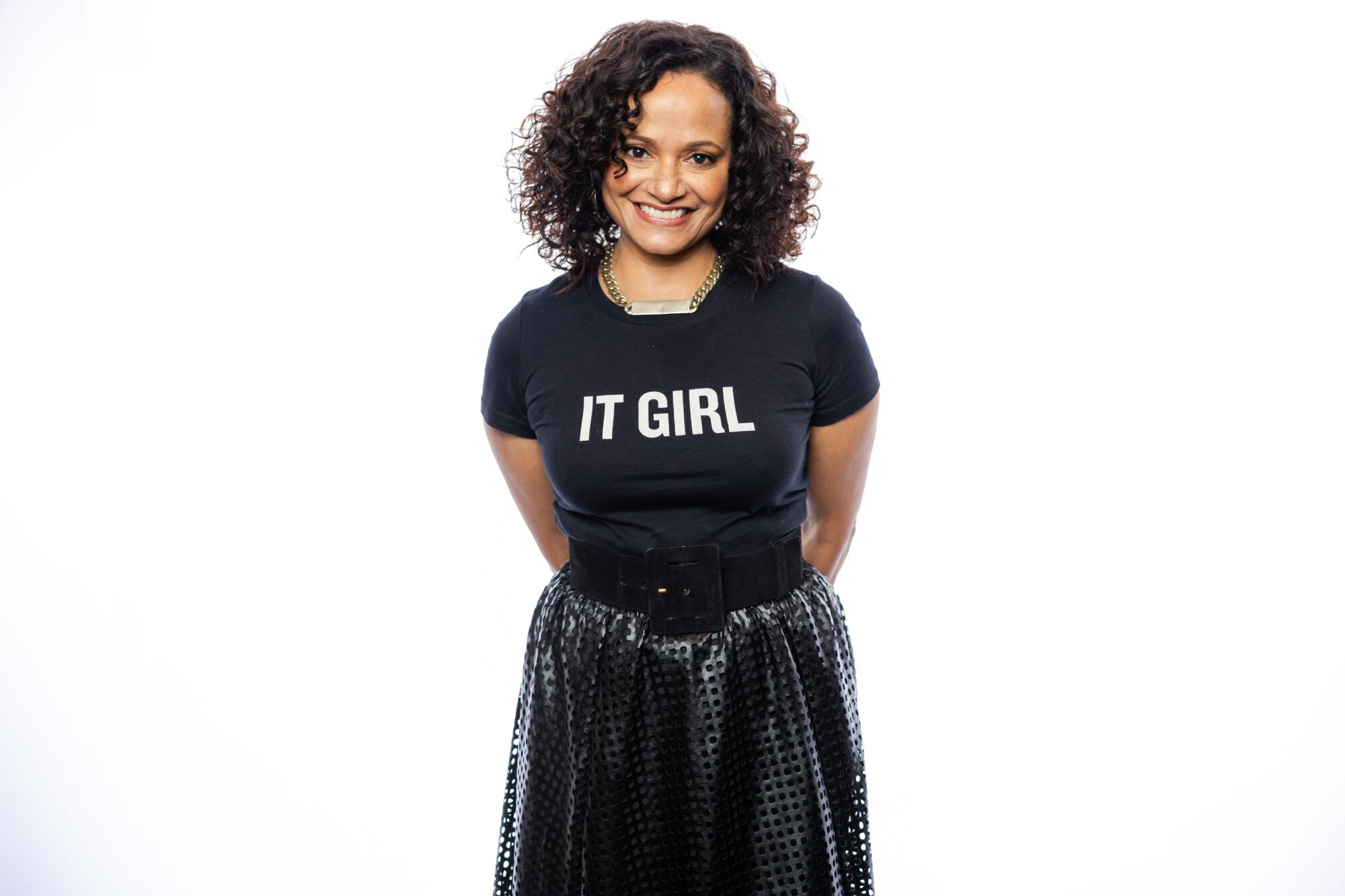 A smiling, standing woman wears a T-shirt with the words "It Girl." 