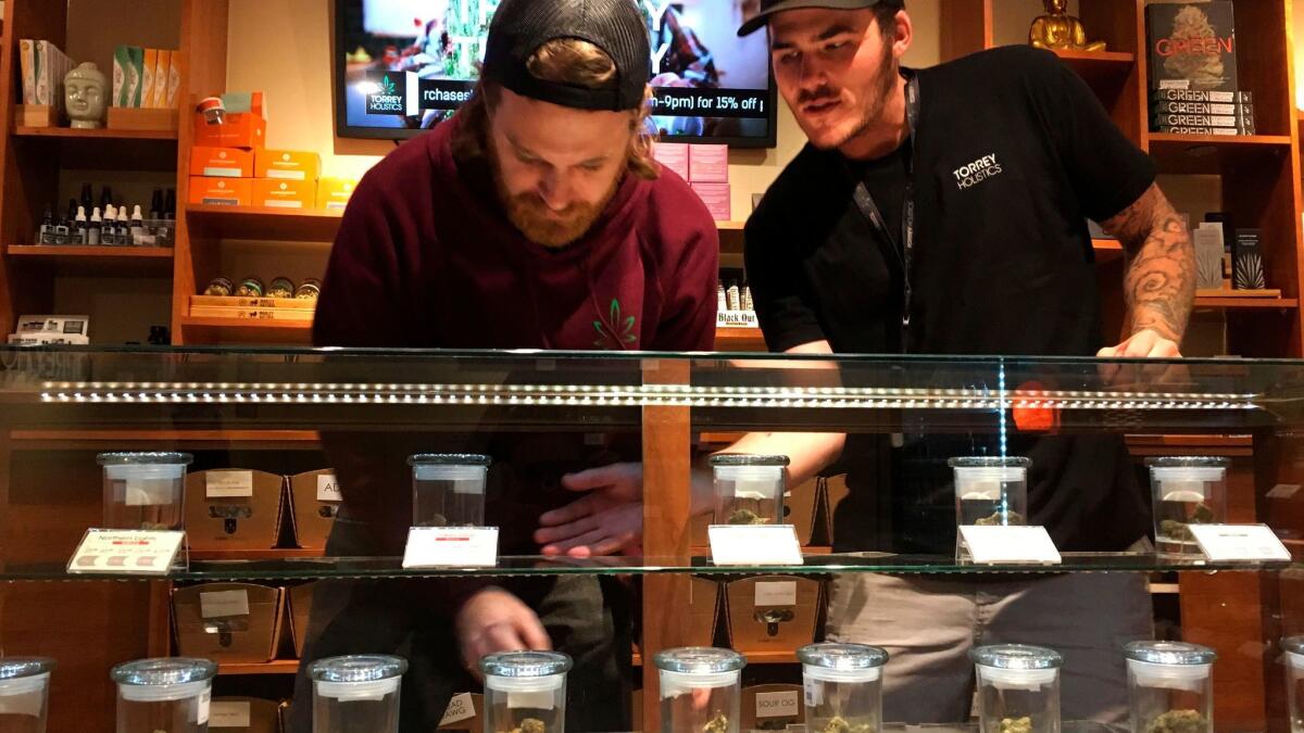 Torrey Holistics employees Matt Sullivan, left, and Taron McElroy arrange jars of cannabis at the San Diego store in December, when it became the first to get a state license to sell marijuana for recreational use.
