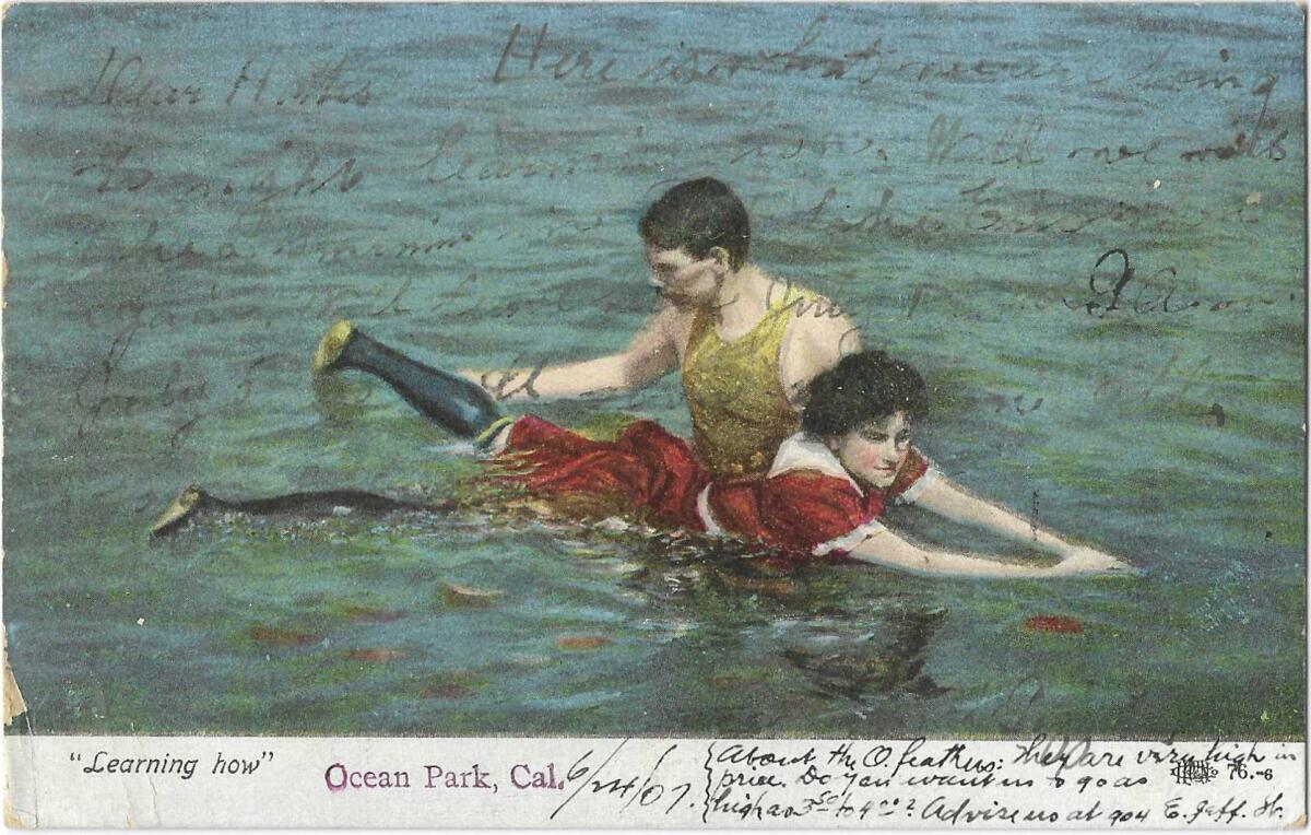 A man helps a woman -- dressed in a red, knee-length bathing suit and black stockings -- learn to swim. 