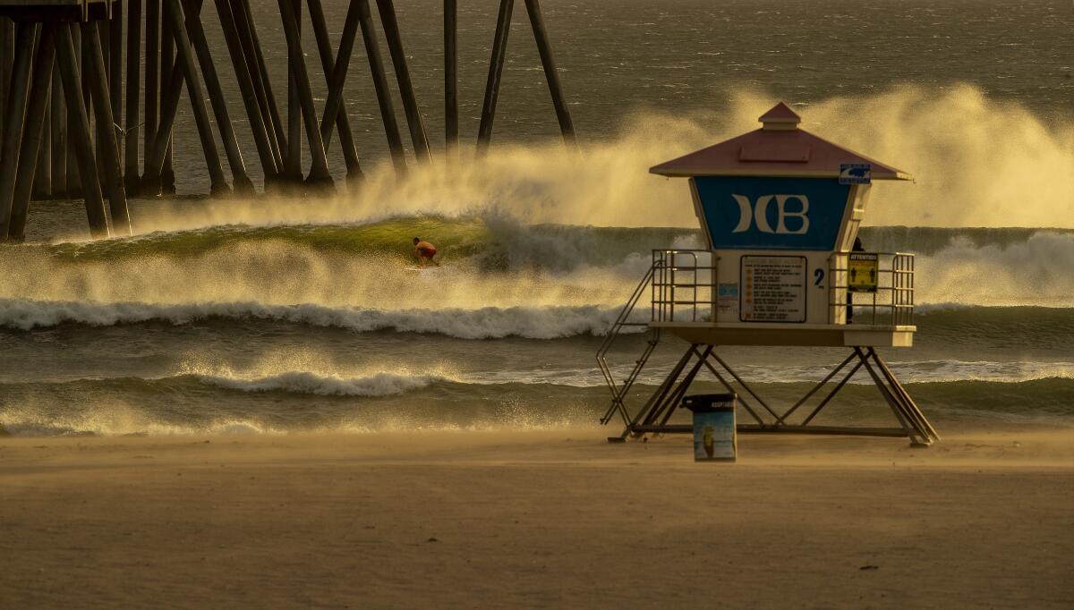 A surfer rides a wave illuminated by the setting sun and sculpted by gusty Santa Ana winds near the Huntington Beach Pier.