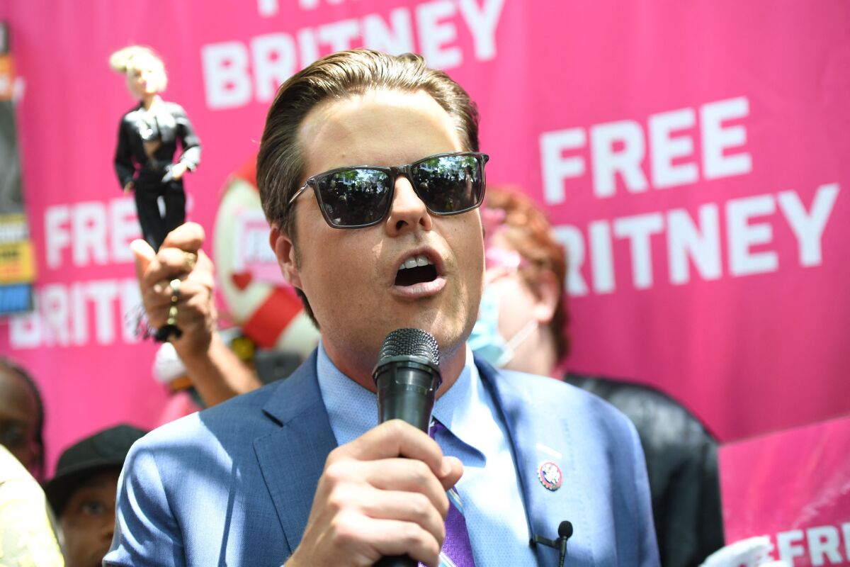 A man in a blue suit speaks into a microphone in front of a pink Free Britney backdrop