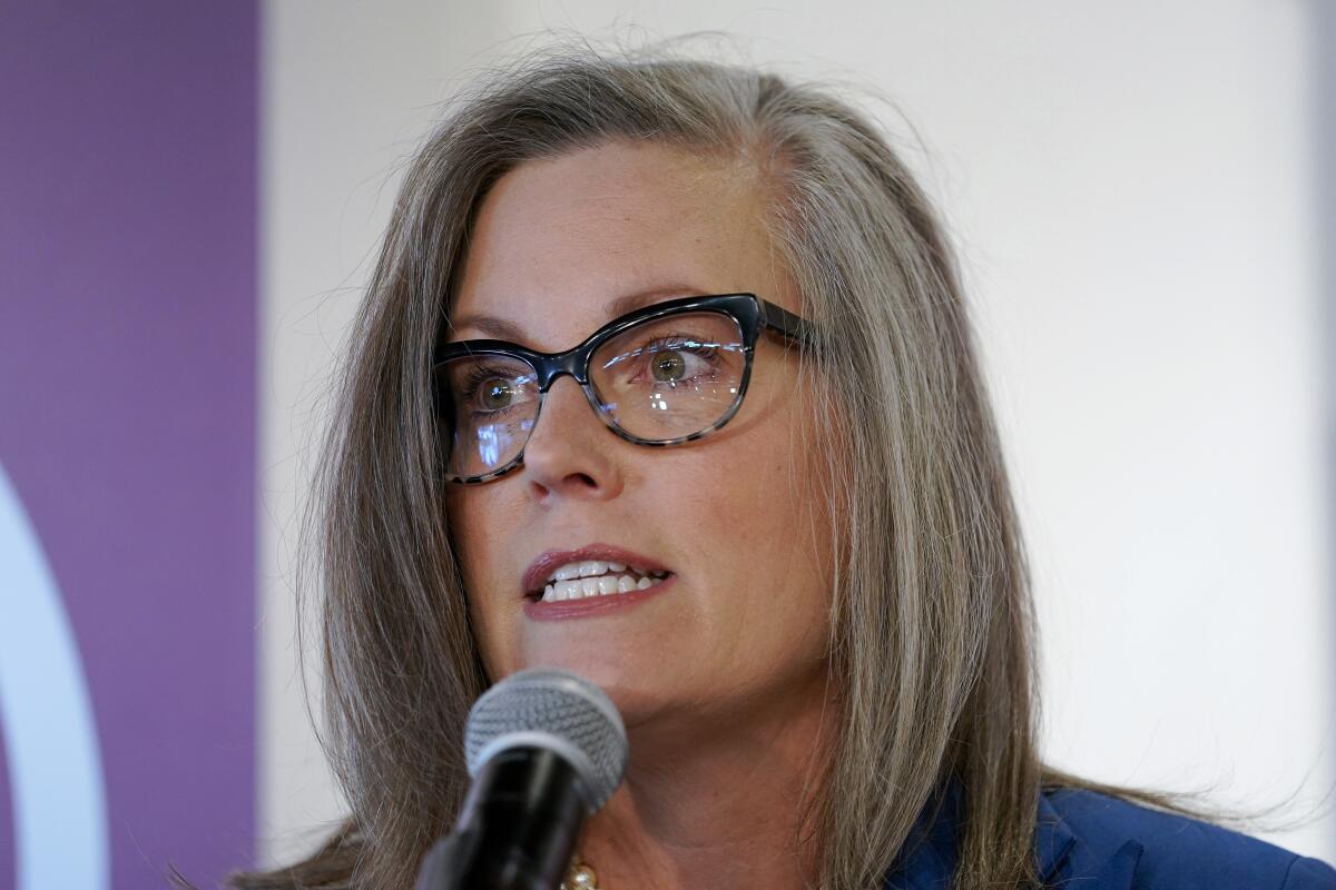 A woman with shoulder-length salt-and-pepper hair and glasses speaks before a microphone 