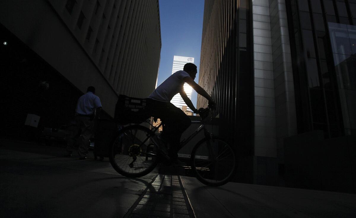 A bicyclist rides through shadows cast by tall buildings along Wilshire Boulevard. Dense development lines the boulevard as it winds from the skyscrapers of downtown Los Angeles to its terminus overlooking the Pacific Ocean in Santa Monica.