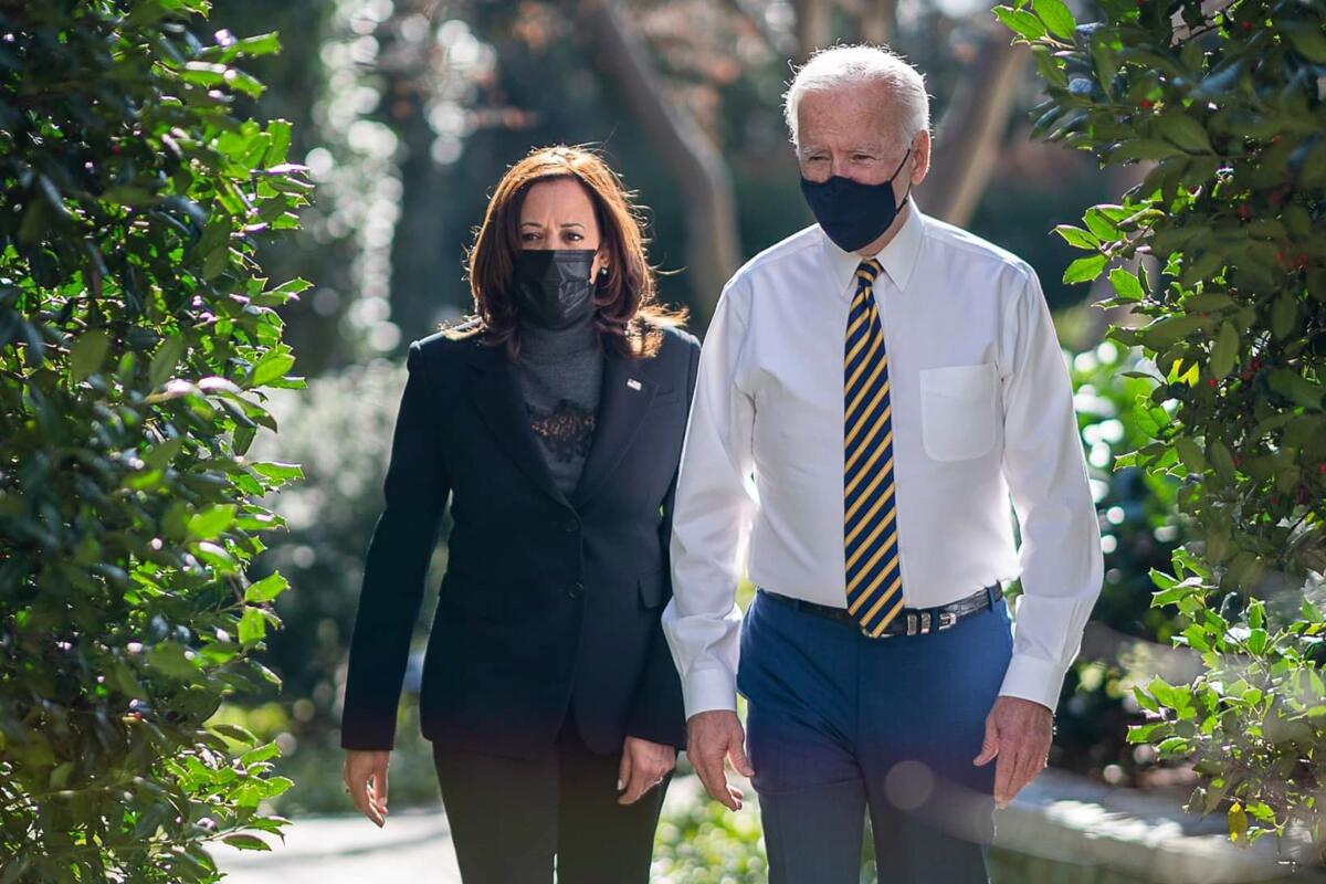 President Biden and Vice President Kamala Harris wear masks and walk outdoors.