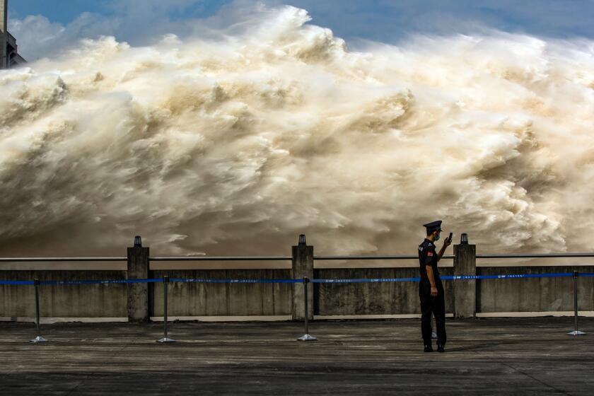 TOPSHOT - This photo taken on July 19, 2020 shows a security guard looking at his smartphone while water is released from the Three Gorges Dam, a gigantic hydropower project on the Yangtze river, to relieve flood pressure in Yichang, central China's Hubei province. - Rising waters across central and eastern China have left over 140 people dead or missing, and floods have affected almost 24 million since the start of July, according to the ministry of emergency management. (Photo by STR / AFP) / China OUT (Photo by STR/AFP via Getty Images)