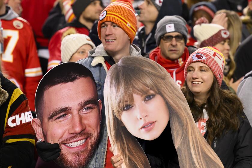 A pair of Kansas City Chiefs fans hold Travis Kelce and Taylor Swift cutouts during an NFL football game