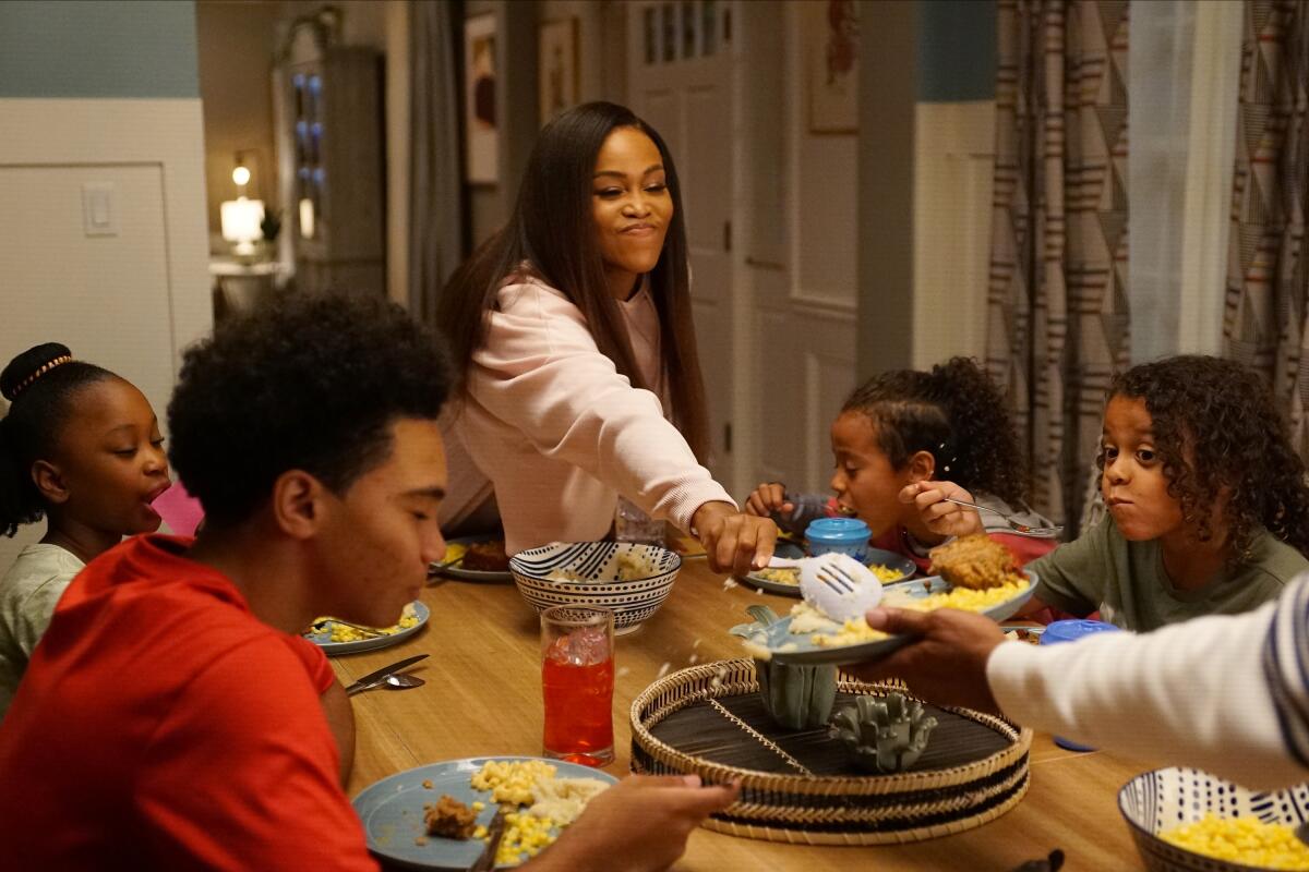 A woman serves food to a family sitting at a dinner table.