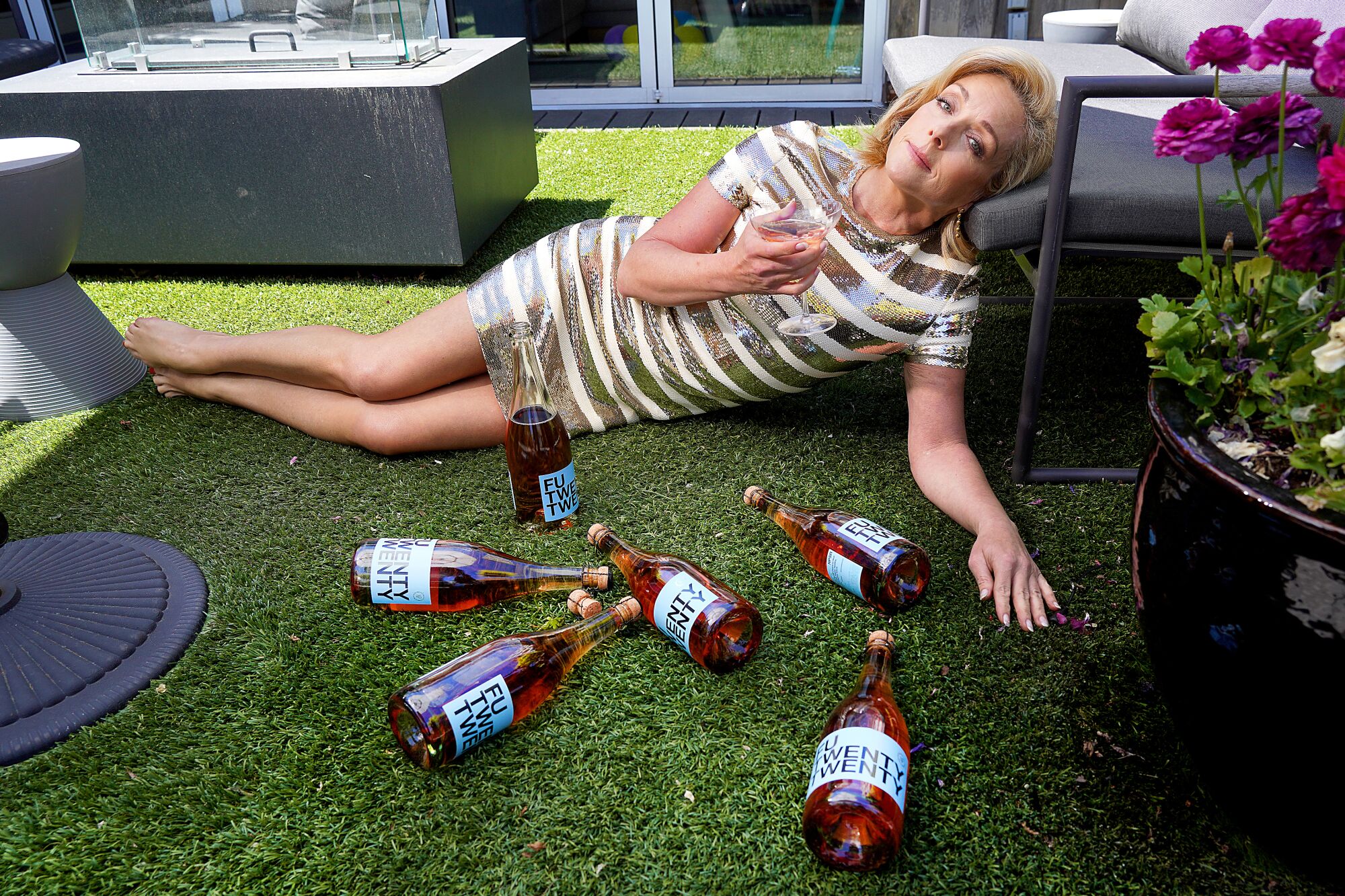 Jane Krakowski poses on fake grass surrounded by wine bottles with fake labels.