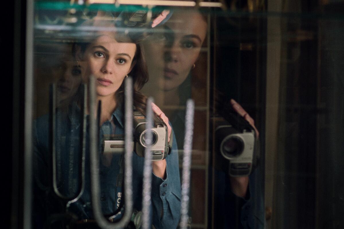 A woman is reflected in a mirror holding a camcorder 