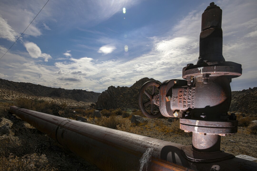 A closeup view of a valve on a water pipe that stretches away into a desert landscape