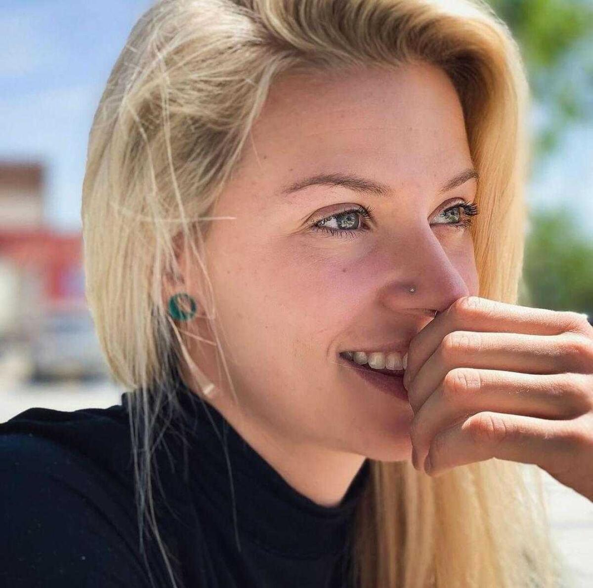 A woman in long blond hair holds her hand to her mouth and smiles.