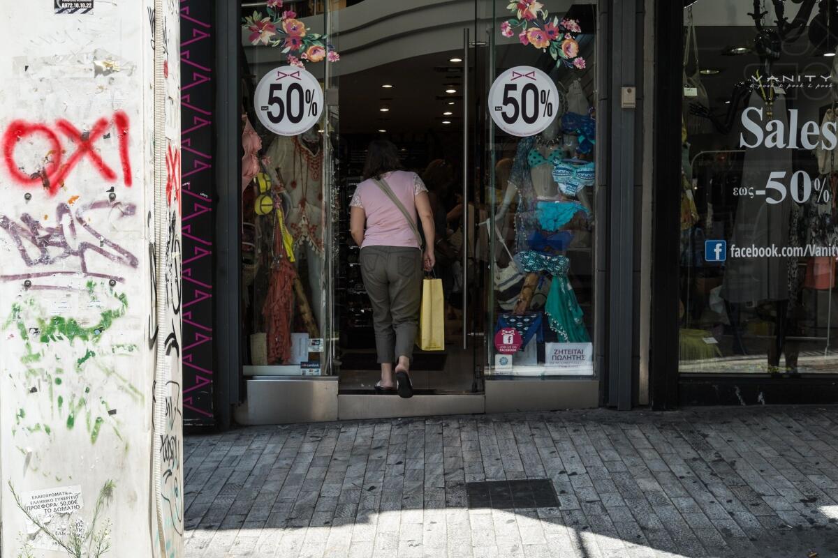 A woman enters a store next to a wall bearing a graffiti reading in Greek "OXI" (NO), in downtown Athens on Tuesday.
