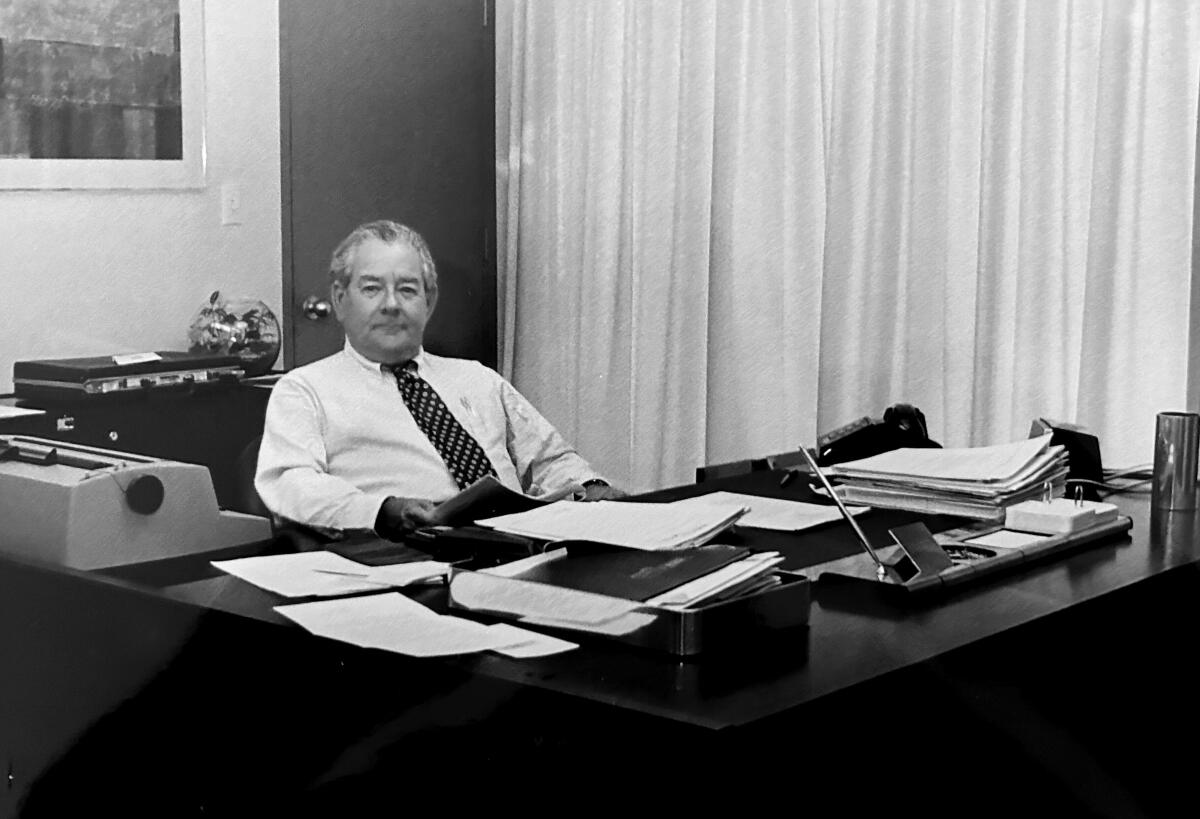 An old black-and-white photo of Ignacio E. Lozano Jr. sitting behind a large desk with a typewriter and neat piles of paper
