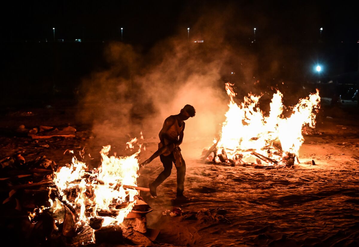 A worker tends to a blazing funeral pyre as another pyre burns nearby