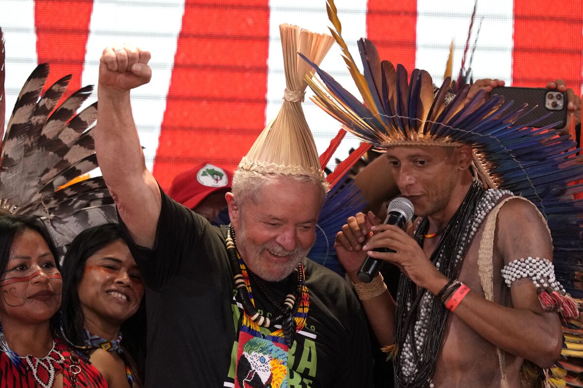 Brazil's former President Luiz Inacio Lula da Silva raises his right fist after receiving a traditional Indigenous headdress during the 18th annual Free Land Indigenous Camp, in Brasilia, Brazil, Tuesday, April 12, 2022. (AP Photo/Eraldo Peres)