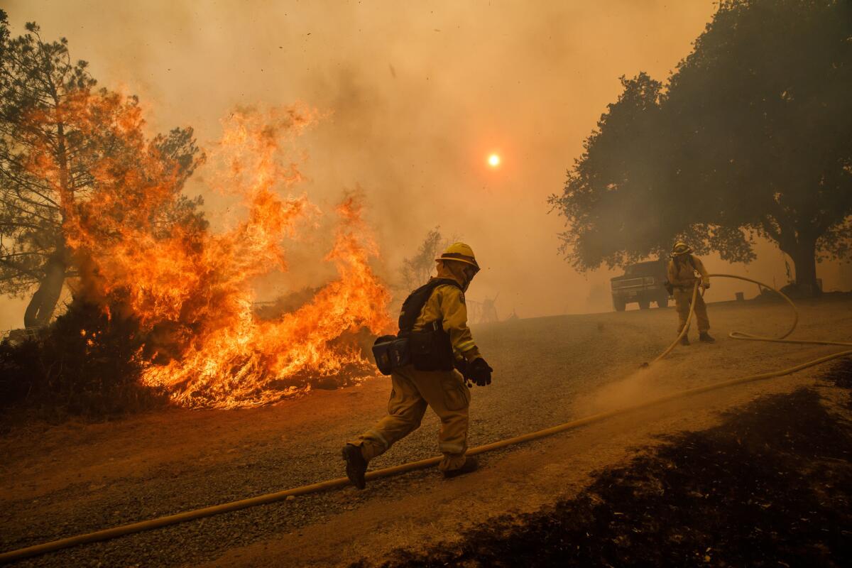 Firefighters work to keep flames from the River fire from destroying a home as evening winds kick in near Lakeport, Calif.