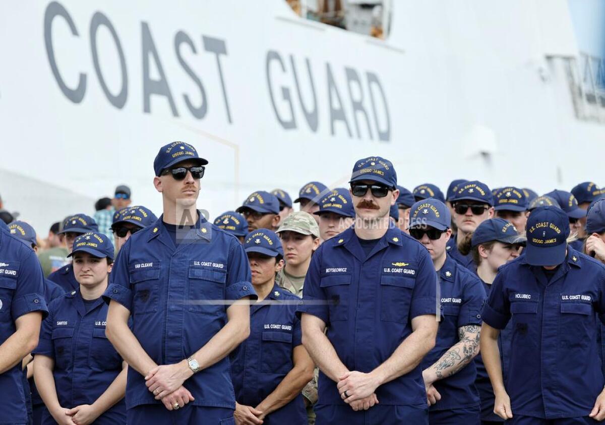 Coast Guard members stand at attention near a ship 