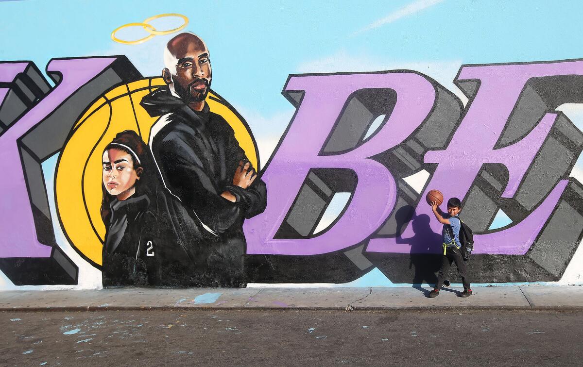 A kid holds a basketball in front of a mural painted in honor of Kobe Bryant and his daughter, Gianna.