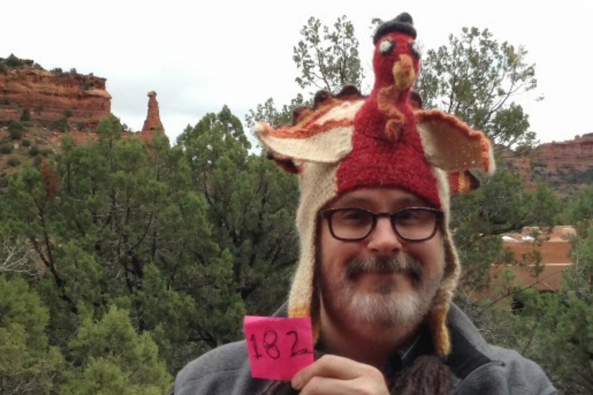 A bearded man wearing a turkey hat with Sedona, Arizona, in the background