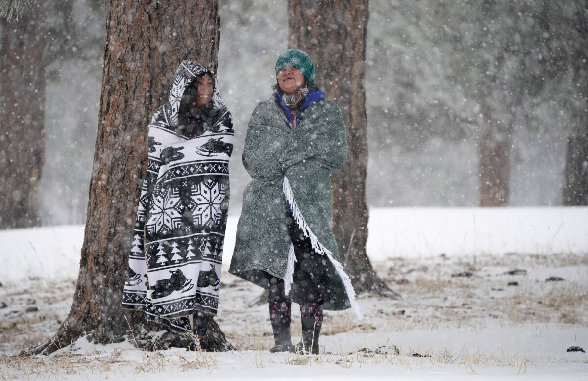 Two women wrapped in blankets as snow falls.