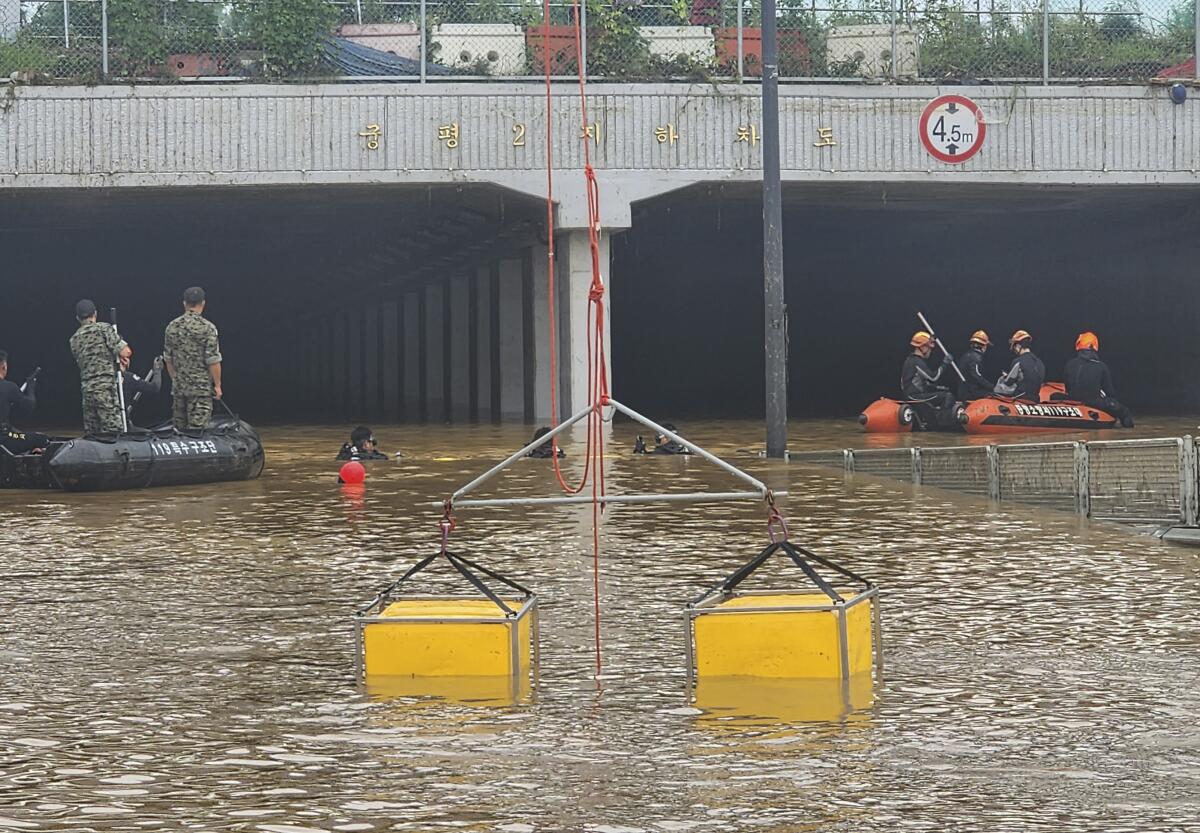 Rescuers in rafts search for survivors along a road submerged by floodwaters leading to an underground tunnel.