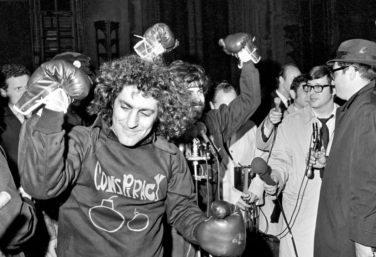 Abbie Hoffman and Jerry Rubin raise their fists, in boxing gloves, and wear shirts that say "Conspiracy." 