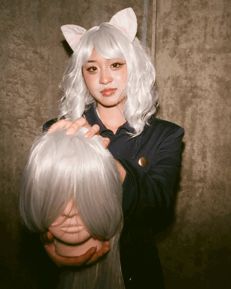 A person wearing a blond wig and cat's ears holds a fake decapitated head also with blond hair.