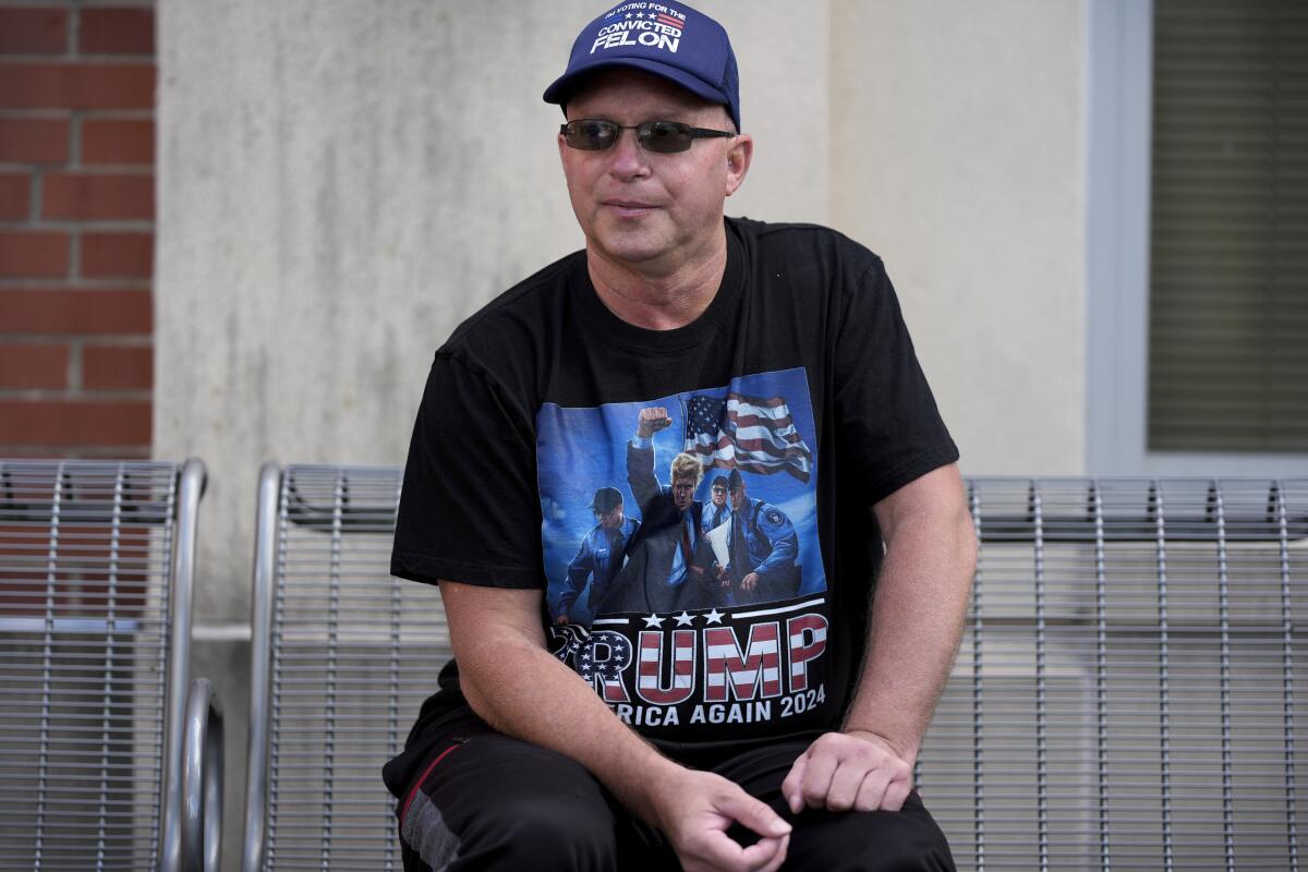 A man in a Trump shirt sitting on a bench speaks