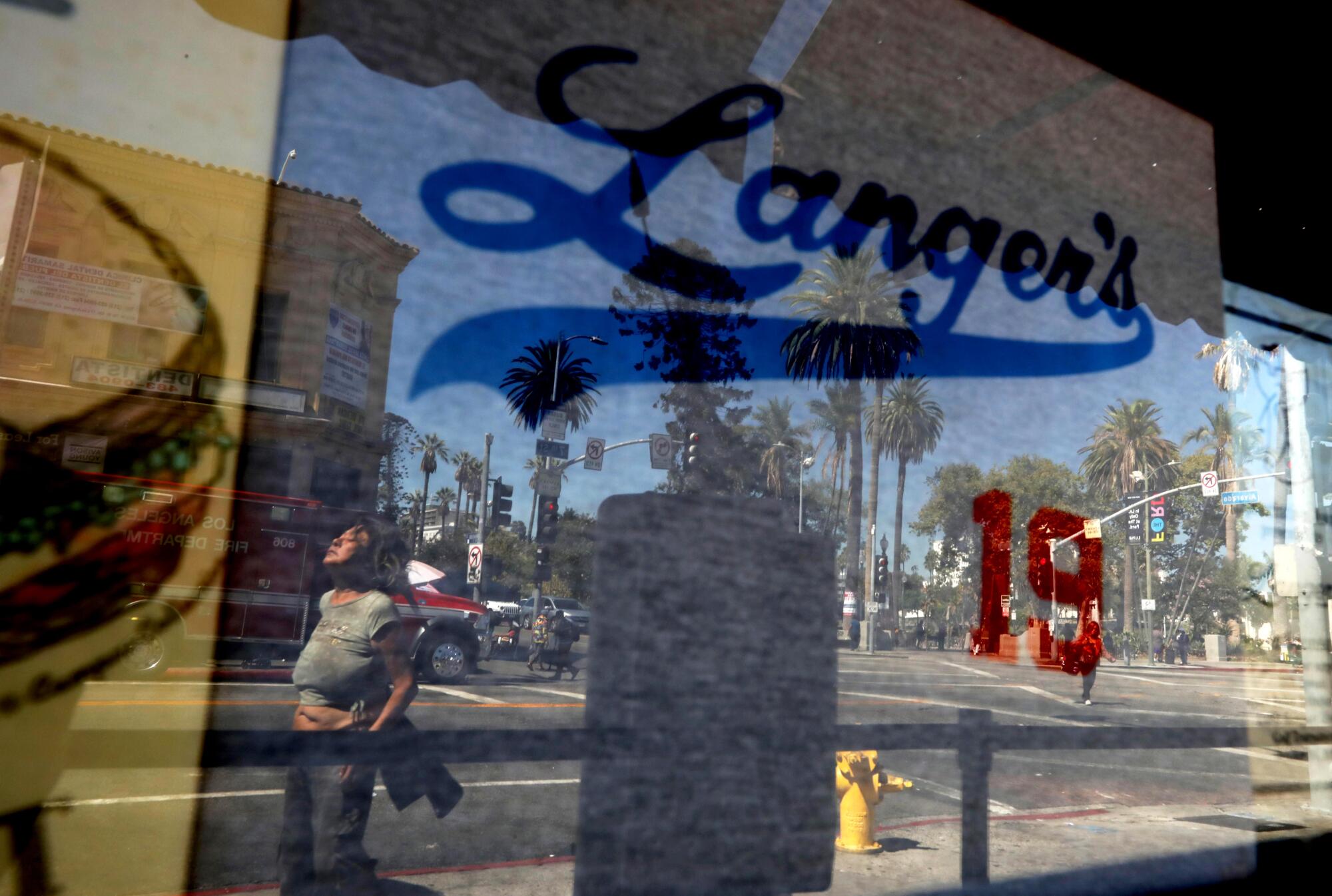 A pedestrian, reflected, walks past the storefront window of Langer's Deli. 