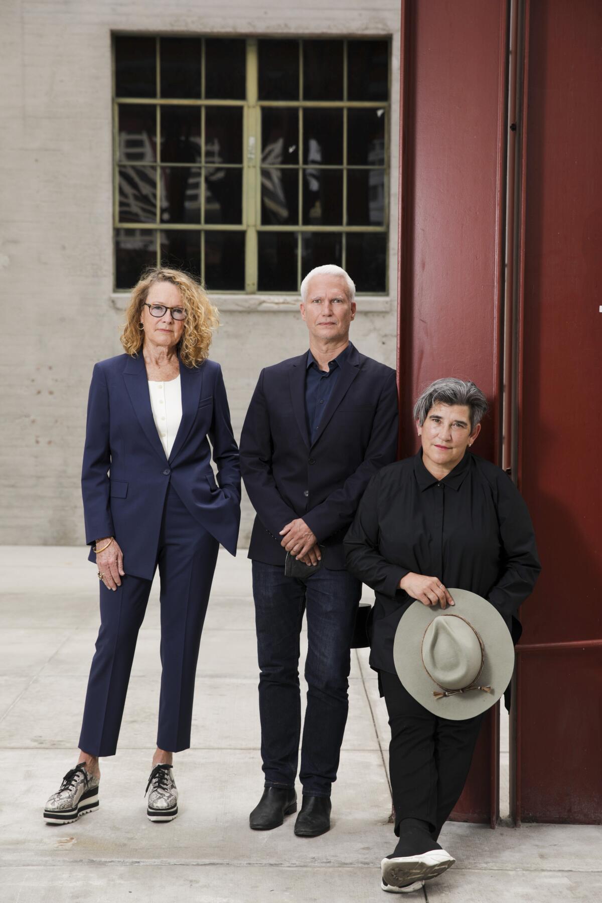 A woman, left, and two men pose outside a building beneath a window