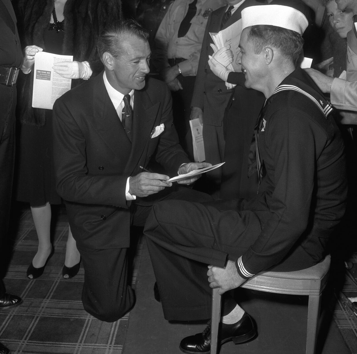 Gary Cooper kneels in front of a chair where a man Navy man is seated.