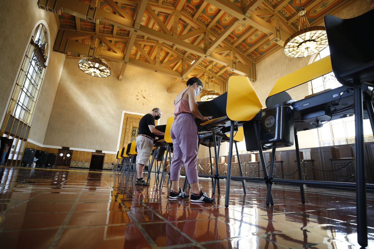 Two people vote at a long row of voting booths in a cavernous space.