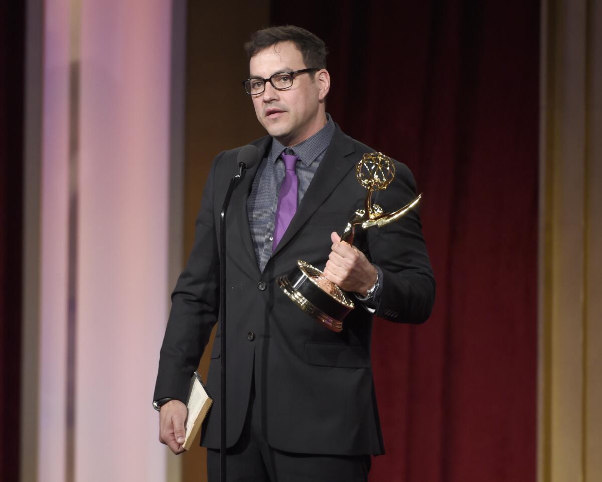 Tyler Christopher holds a Daytime Emmy Award in one hand onstage in a dark suit and purple tie
