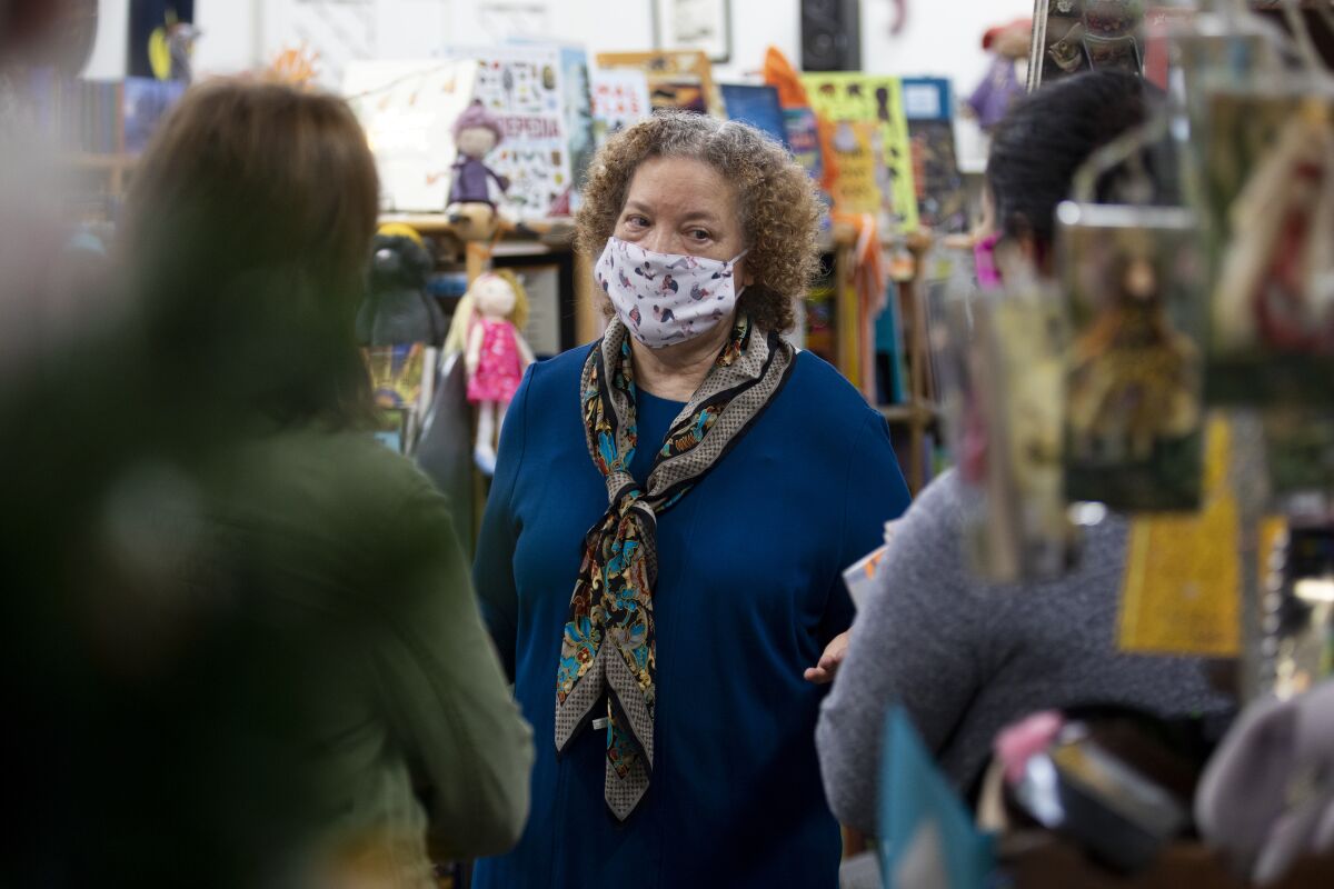 Maureen Palacios, owner of Once Upon a Time, stands in her bookstore wearing a mask and talking with customers.