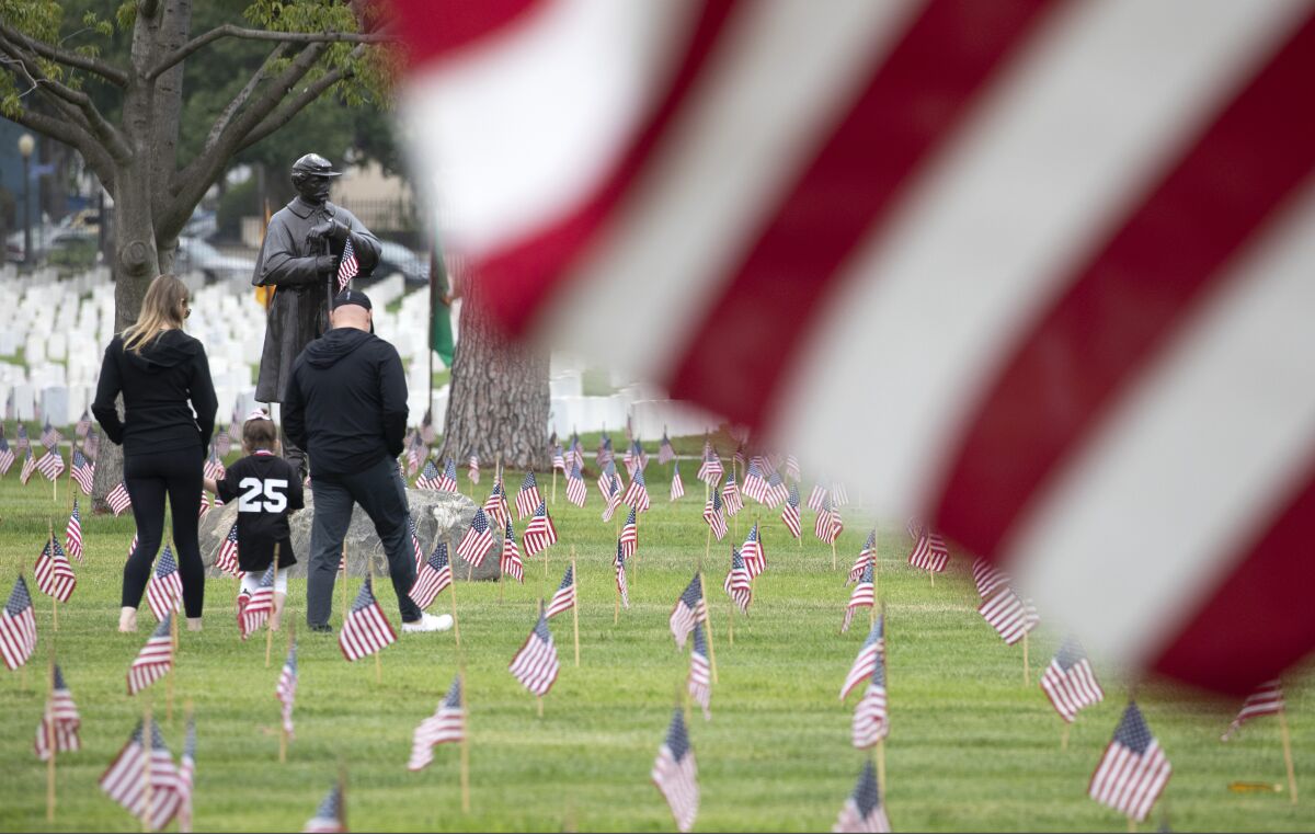 A woman, child and man walk among small flags planted at Los Angeles National Cemetery in 2021 for Memorial Day.