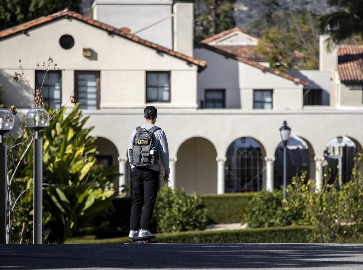A student wearing a backpack stands in front of a college building.  