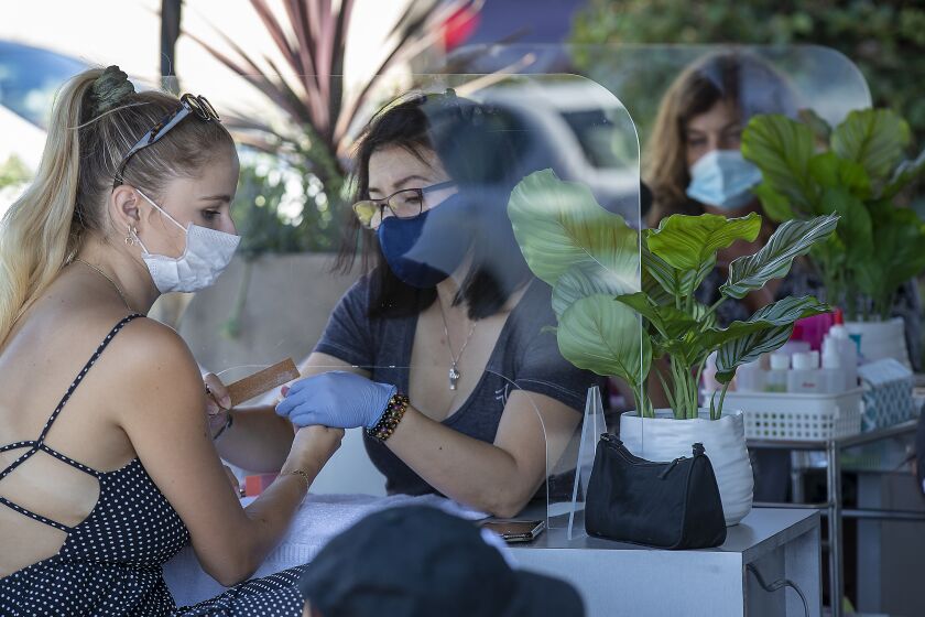 TUSTIN, CA - JULY 22: Beauty technicians wear face masks as they give clients wearing face masks manicures and pedicures outdoors, as mandated by Gov. Newsom on Monday, in front of their Ritz Nails business at The District Tustin Legacy in Tustin Wednesday, July 22, 2020. (Allen J. Schaben / Los Angeles Times)
