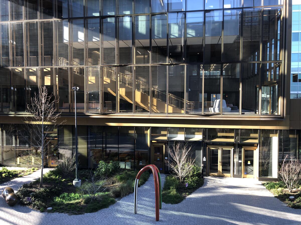 Seen from outside, the atrium of a glass building with a descending wooden staircase.