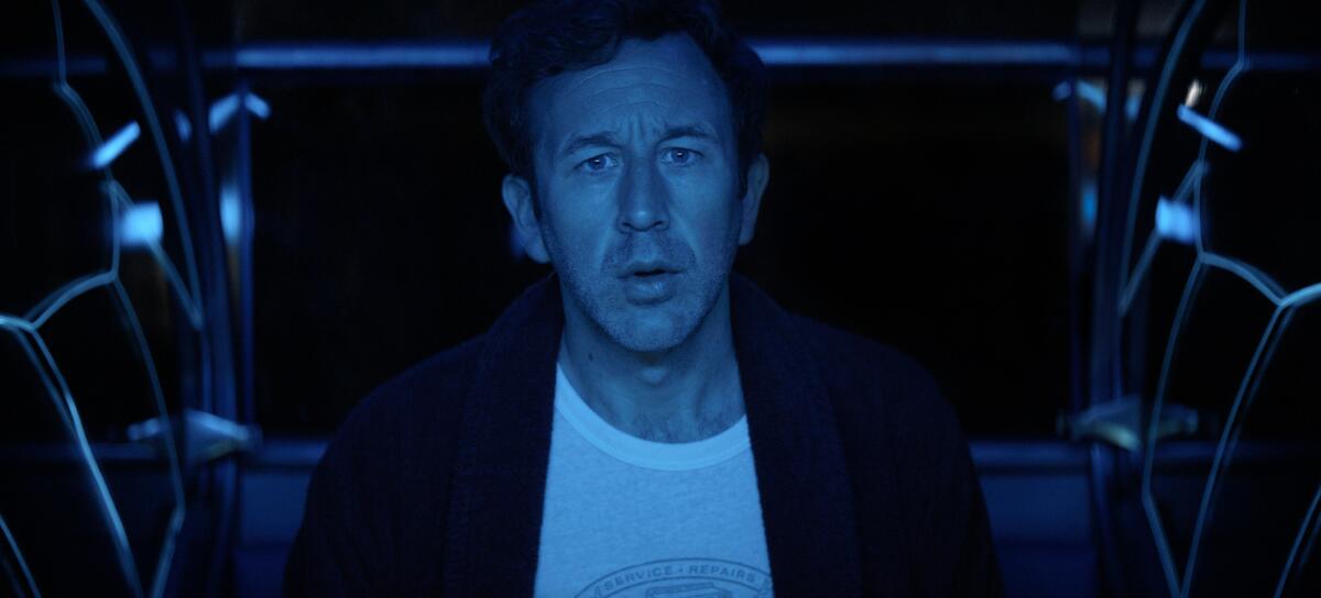 A man cast in blue light stares ahead.