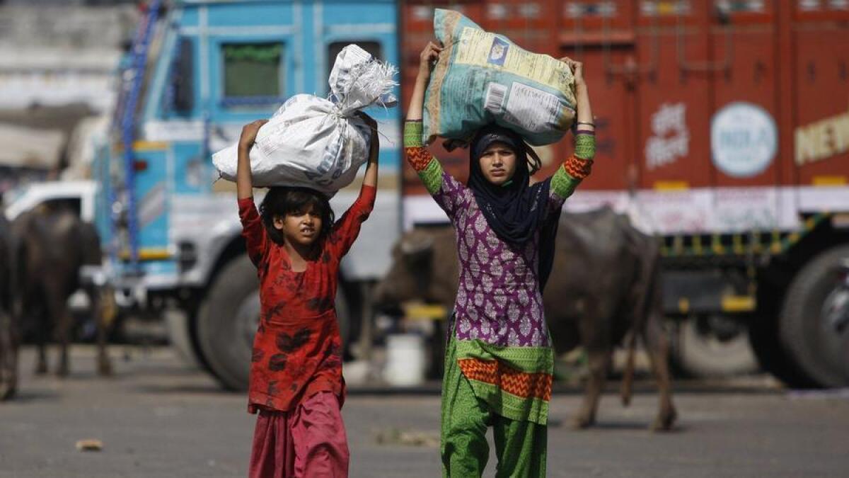 In this 2015 photo, Indian child laborers carry sacks of vegetable leftovers collected from a wholesale market to sell in their shantytown on the outskirts of Jammu, India.