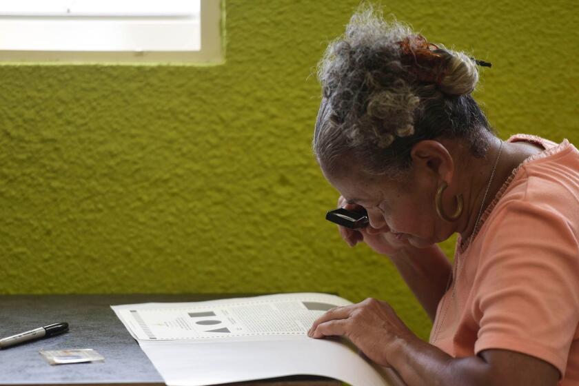 Puerto Rican resident Marla Quinones looks carefully at her ballot with a magnifying glass before voting during the fifth referendum on the island's status, in San Juan, Puerto Rico, Sunday, Jun. 11, 2017. Puerto Ricans are getting the chance to tell U.S. Congress ultimately has to approve the outcome of Sunday's referendum that offers voters three choices: statehood, free association/independence or current territorial status. (AP Photo/Carlos Giusti)