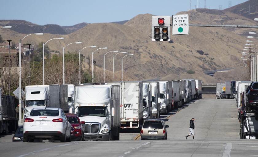 A line of big rigs are parked alongside a road.